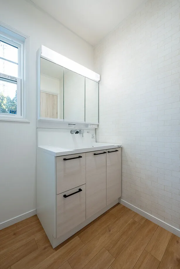 白を基調とした清潔感のある洗面脱衣室。レンガ調のアクセントクロスや木目調の面材など、主張しすぎないシンプルなデザインを採用されました。お風呂と同様に、窓の外の景色に癒されながら身支度を整えることが可能です。