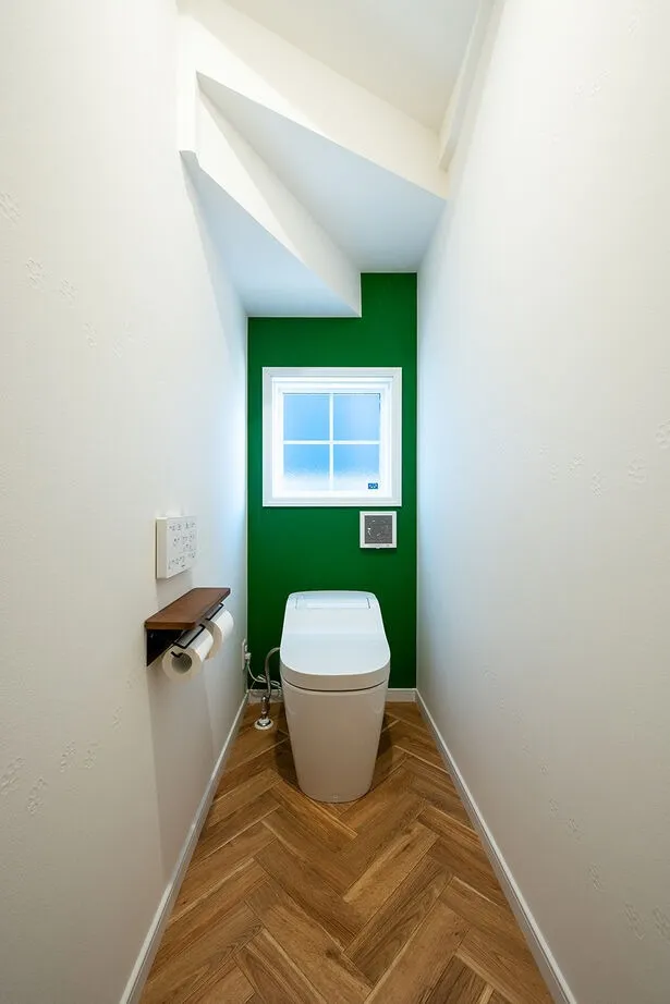1階のトイレは階段下のスペースを無駄なく活用。鮮やかなグリーンのアクセントクロスとヘリンボーン柄の床で、他の空間とは違ったカジュアルな印象に仕上げた。一見シンプルなサイドのクロスは、猫の足跡がエンボス加工されたものを使用している